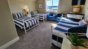 Quarto com duas camas de solteiro, uma escrivaninha, uma cadeira, televisão e janela com cortinas.