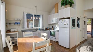 A compact kitchen with white cabinets, a wooden dining table, and a refrigerator. - Sand Dollar- Adorable 2 bedroom  with a Hot tub, fenced yard, BBQ and pets ok . (Ocean Shores)