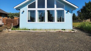 A light blue single-story building with a gabled roof and six large windows. - Sand Dollar- Adorable 2 bedroom  with a Hot tub, fenced yard, BBQ and pets ok . (Ocean Shores)