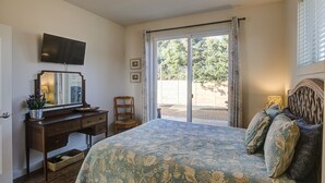 A bedroom with a bed, a desk with a mirror, a chair, and a television on the wall. - Sand Dollar- Adorable 2 bedroom  with a Hot tub, fenced yard, BBQ and pets ok . (Ocean Shores)