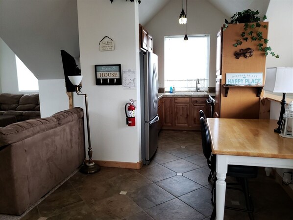 A compact kitchen with a refrigerator, sink, and wooden cabinets. There's a fire extinguisher on the wall and a sign that reads "Welcome to our Happy Place."
