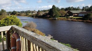 Blick auf einen Fluss mit einer Holzterrasse, einem Rettungsring und einem kleinen Steg.