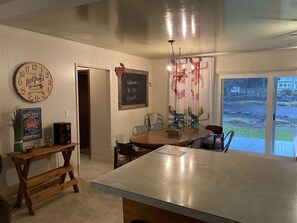A dining area with a large island, a round wall clock, and a chalkboard sign. - Joe Creek Inn- Unique Home (Pacific Beach)