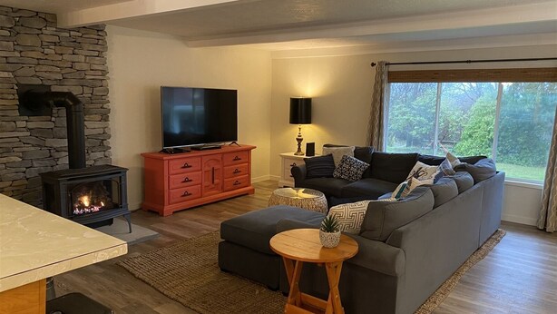 A modern living room with a stone fireplace, a television, a sofa, and a dining area. - Joe Creek Inn- Unique Home (Pacific Beach)