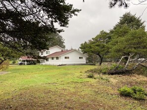 A two-story white house with a red roof, surrounded by a grassy yard and trees. - Joe Creek Inn- Unique Home (Pacific Beach)