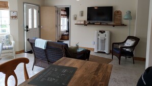 Een gezellige woonkamer met een houten eettafel, rieten stoelen, een flatscreen televisie en een plafondventilator.