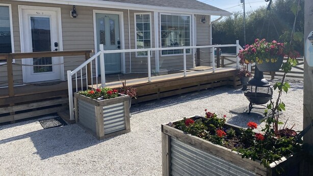 Een laag gebouw met een overdekte veranda, een klein terras en een tuin met bloembedden.