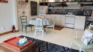 Een kleine keuken met witte kastjes, een eettafel met stoelen en een kleine koelkast.