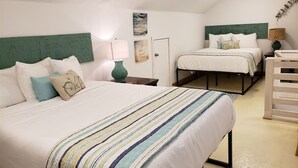 Een slaapkamer met twee bedden, een groen hoofdeinde, een gestreept dekbed en een klein tafeltje met een lamp.