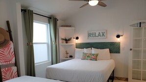 Ein Schlafzimmer mit zwei Betten, einem Deckenventilator, einem Schild mit der Aufschrift 'RELAX' und einer Tür mit Milchglasfenstern.