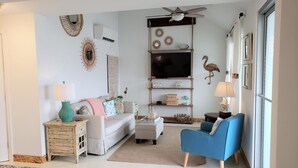 Ein Wohnzimmer mit einer Couch, einem blauen Sessel, einem Fernseher und Wandbildern.