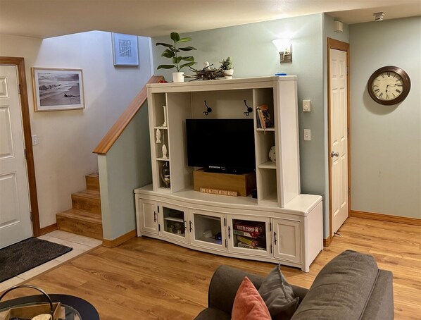 Een woonkamer met een witte entertainmentkast, een televisie en een klok aan de muur.