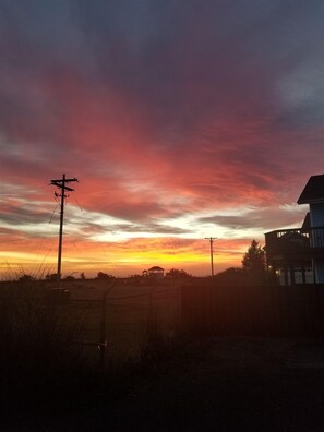 Un coucher de soleil sur un paysage rural, avec une maison et des poteaux électriques.