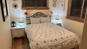 Ein Schlafzimmer mit einem Bett, zwei Nachttischen, einem Fenster mit Jalousien und Wanddekorationen.