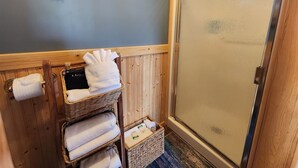 A bathroom with wooden walls, a glass shower door, and a towel rack with folded towels. - Moss Landing # 3 Studio (Ocean Shores)