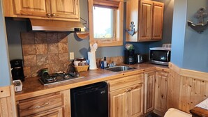 A kitchen with wooden cabinets, a gas stove, a dishwasher, a microwave, and a window with a view. - Moss Landing # 3 Studio (Ocean Shores)