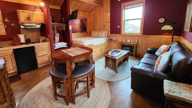 A cozy cabin interior with a wooden ceiling, a dining area with a round table and chairs, a sofa, a bed, and a kitchen area. - Moss Landing # 4 Studio (Ocean Shores)