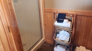 A corner of a room with a wooden door and a small wooden shelf holding folded towels and a black towel with "Makeup" written on it. - Moss Landing # 4 Studio (Ocean Shores)