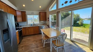 A modern kitchen with wooden cabinets, a stainless steel refrigerator, and a dining area with a wooden table and white chairs. - The Lake House - Best of both worlds (Ocean Shores)