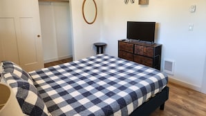 A bedroom with a checkered bedspread, a TV on a wooden dresser, and skis and a paddleboard on the wall. - The Lake House - Best of both worlds (Ocean Shores)