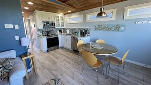 A compact kitchen with modern appliances, a dining area with a round table and chairs, and a cozy seating area with a sofa. - Moclips Sand Dollar Beach House - Beautiful Beach Front Home (Moclips)