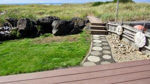 A wooden deck with a stone pathway leading to a wooden fence with decorative elements. - Moclips Sand Dollar Beach House - Beautiful Beach Front Home (Moclips)