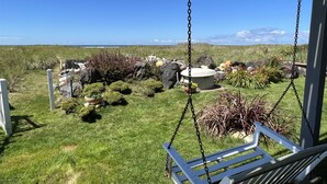 A garden with a swing chair overlooking a grassy area with rocks and plants, and a view of the ocean. - Moclips Sand Dollar Beach House - Beautiful Beach Front Home (Moclips)