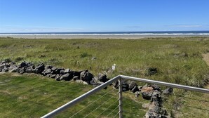 Un champ d’herbe, avec une barrière métallique au premier plan, qui mène à une plage où l’on aperçoit des vagues à l’arrière-plan.