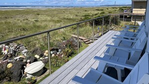 Une terrasse dotée de chaises longues, donnant sur une plage et offrant une vue sur l’océan et les montagnes lointaines.