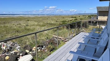 A deck with lounge chairs overlooking a beach with a view of the ocean and distant mountains.
