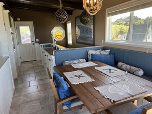 A cozy dining area with a wooden table, blue upholstered bench, and decorative wall art. - Captain`s Quarters - Beautifully Updated Beach Front Home (Moclips)