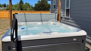 A hot tub under a wooden pergola, with a house in the background.