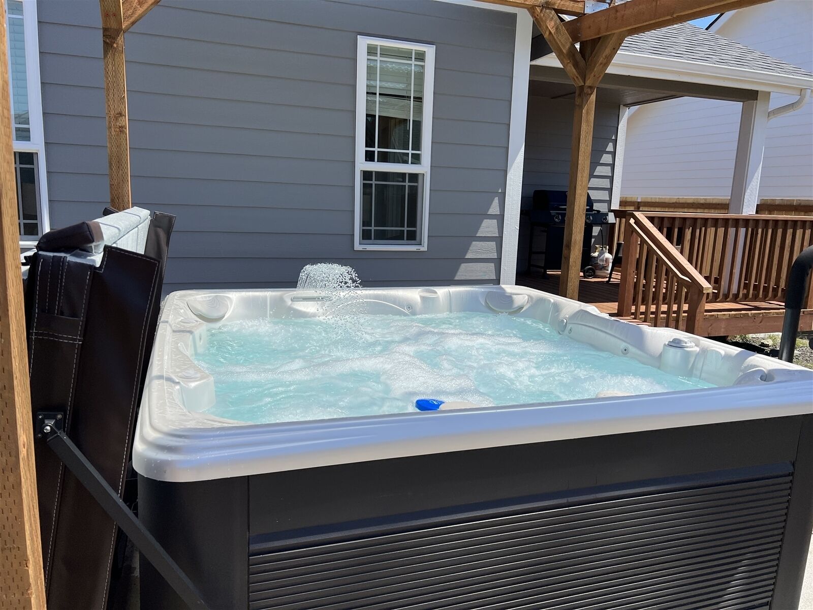A hot tub in a backyard with a wooden deck and a house in the background.