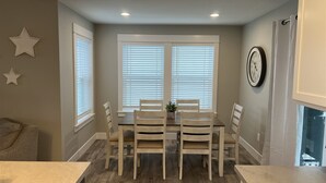 A dining area with a table and chairs, large windows with blinds, a clock on the wall, and a star decoration.