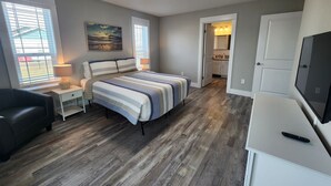 A bedroom with a bed, a nightstand, a lamp, a TV, and a view of the bathroom.