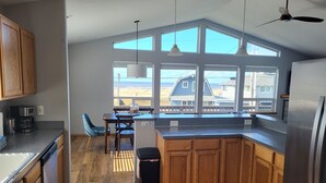 Eine moderne Küche mit Holzschränken, einem Edelstahlkühlschrank und einem großen Fenster mit Blick auf einen Strand.