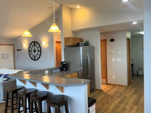 A modern kitchen with a central island, bar stools, a refrigerator, and pendant lighting. - Sea Smoke - Ocean View Home (Moclips)