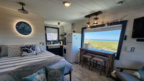 A bedroom with a bed, a desk, and a view of the beach. - Beachcombers Cabin - Ocean Front with Hot Tub (Moclips)