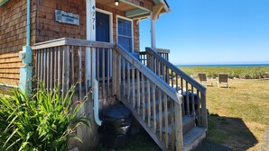 A wooden building with a porch, a staircase, and a view of the ocean. - Beachcombers Cabin - Ocean Front with Hot Tub (Moclips)
