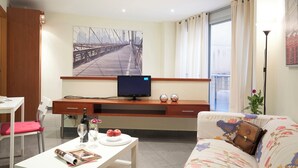 A modern living room with a flat-screen TV, a dining table with a magazine, a sofa with a patterned cover, and a large window with curtains. - BeBarceloner Studios minutes from Pl Universidad (Barcelona)