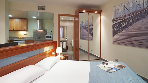 A hotel room with a bed, bedside table, lamp, and a large mirror. There is a bathroom visible through an open door. - BeBarceloner Studios minutes from Pl Universidad (Barcelona)