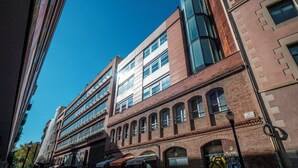 A multi-story building with a mix of brick and glass facades, featuring large windows and a prominent entrance with a sign. - BeBarceloner Studios minutes from Pl Universidad (Barcelona)