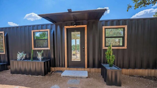 A modern, compact building with a dark exterior, large windows, and a central door. - Contained in Gruene! Hot Tub! (New Braunfels)
