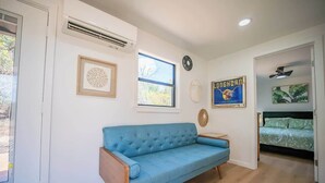 A room with a blue sofa, a bed with a green bedspread, a wall clock, and a framed picture. - Contained in Gruene! Hot Tub! (New Braunfels)