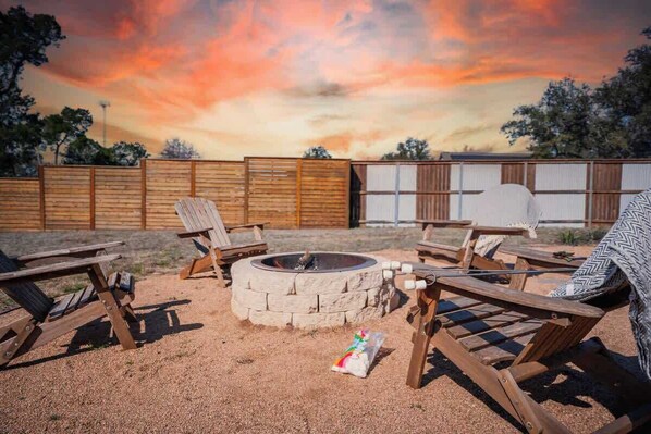 A backyard with a fire pit, wooden chairs, and a wooden fence. - Contained in Gruene! Hot Tub! (New Braunfels)