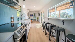 A modern kitchen with a central island, bar stools, and a view through the windows. - Contained in Gruene! Hot Tub! (New Braunfels)