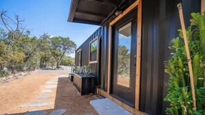 A modern building with large windows, a stone pathway leading to the entrance, and a variety of plants around the property. - Contained in Gruene! Hot Tub! (New Braunfels)