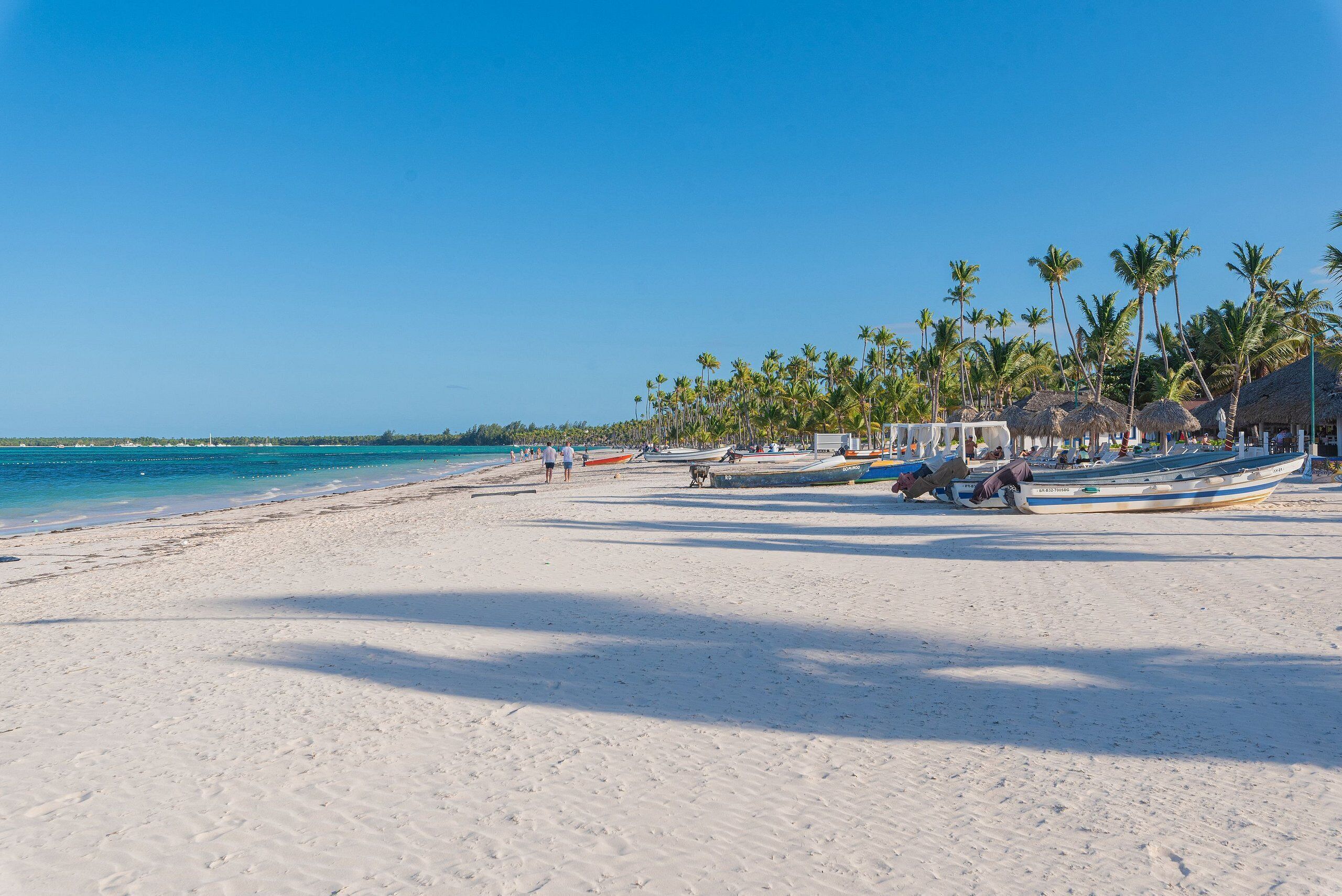 A beach with white sand, palm trees, and boats.
