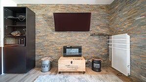 A compact living space with a brick wall, a mounted TV, a wooden chest, and a white refrigerator. - Studio 2/4 ppl near the ski runs (Allos)