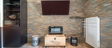 Un espacio habitable pequeño con pared de ladrillo, televisor montado, cofre de madera y refrigerador blanco.